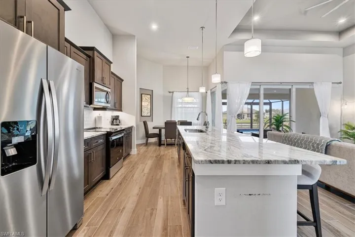 Kitchen with appliances with stainless steel finishes, light wood finished floors, a breakfast bar area, dark brown cabinets, and a center island with sink