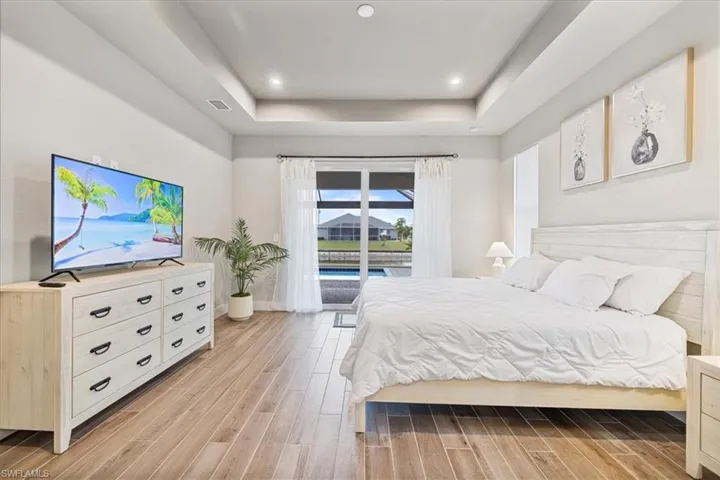 Bedroom with a raised ceiling, access to exterior, light wood finished floors, and recessed lighting