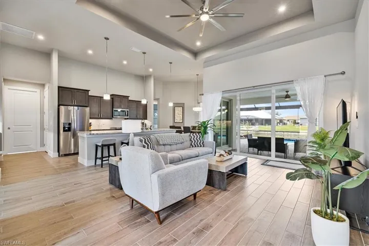 Living area featuring a high ceiling, ceiling fan, a raised ceiling, light wood-style floors, and recessed lighting