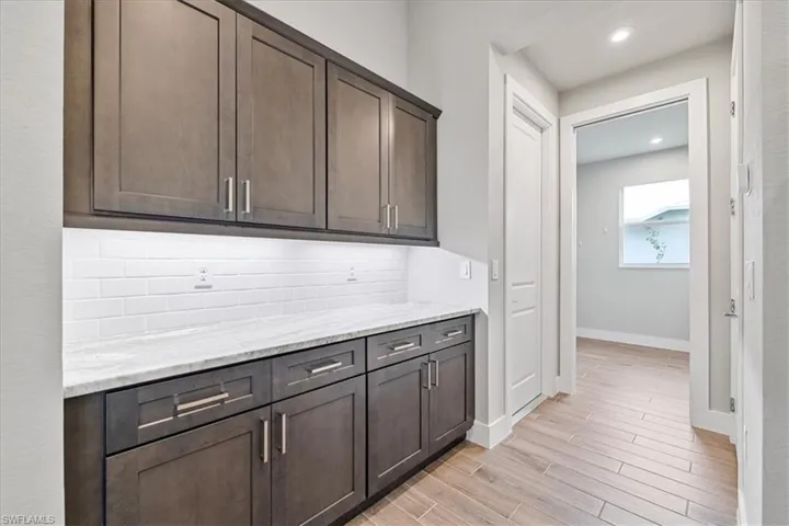 Kitchen featuring dark brown cabinetry, light wood finished floors, tasteful backsplash, light stone countertops, and recessed lighting