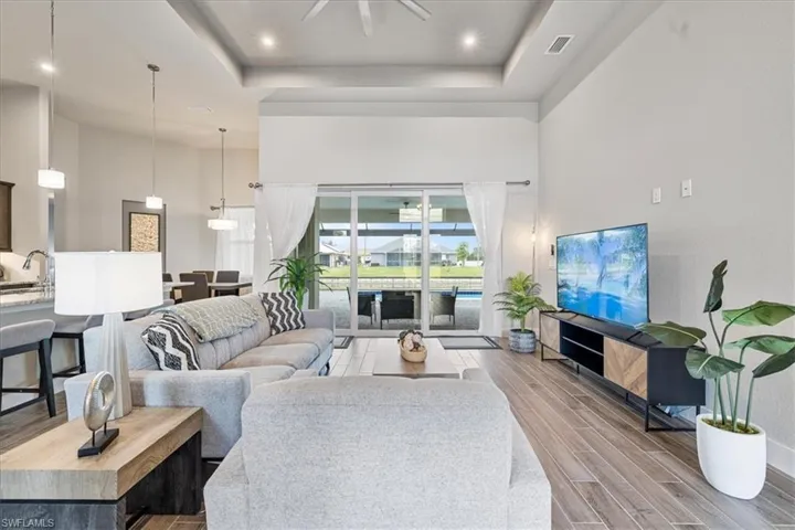Living area featuring a high ceiling, wood finished floors, a raised ceiling, a ceiling fan, and recessed lighting
