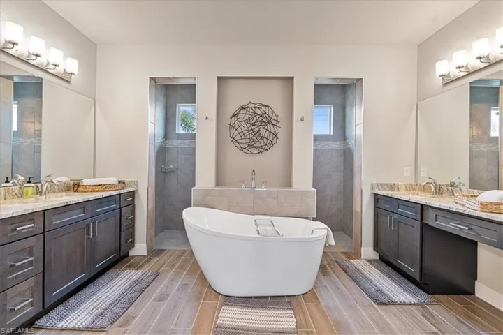Bathroom featuring two vanities, a freestanding bath, a walk in shower, and wood finish floors