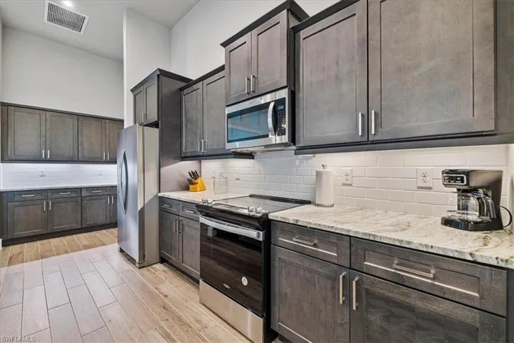 Kitchen with appliances with stainless steel finishes, light wood-style flooring, decorative backsplash, light stone counters, and dark brown cabinetry