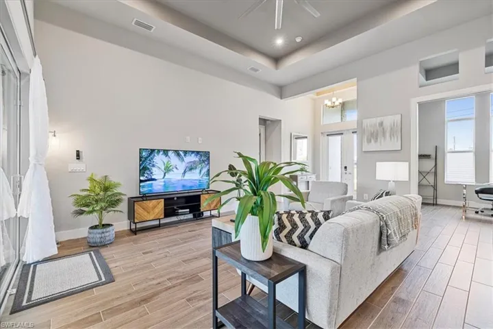 Living area with light wood-style flooring, a chandelier, a tray ceiling, and ceiling fan