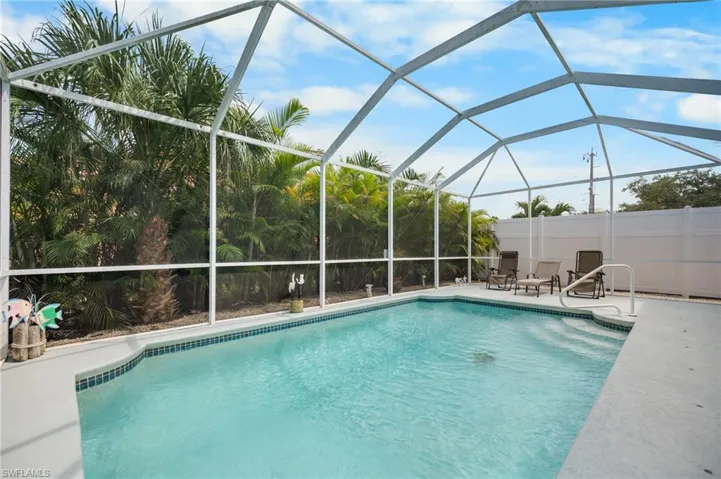 Screened-in swimming pool with a tiled border and integrated steps, surrounded by a concrete deck