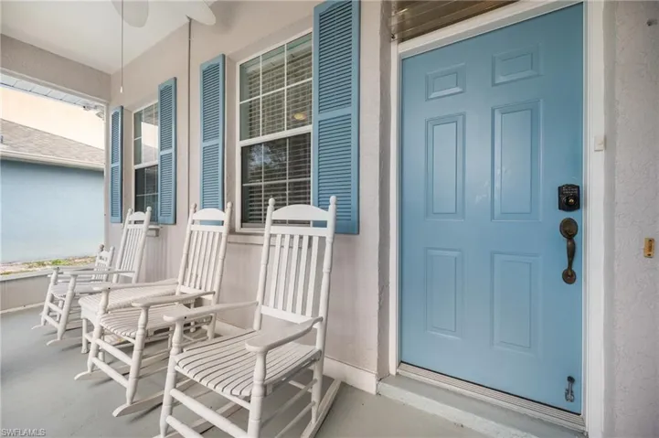 Covered front porch with a blue paneled door, blue louvered shutters, and multiple windows