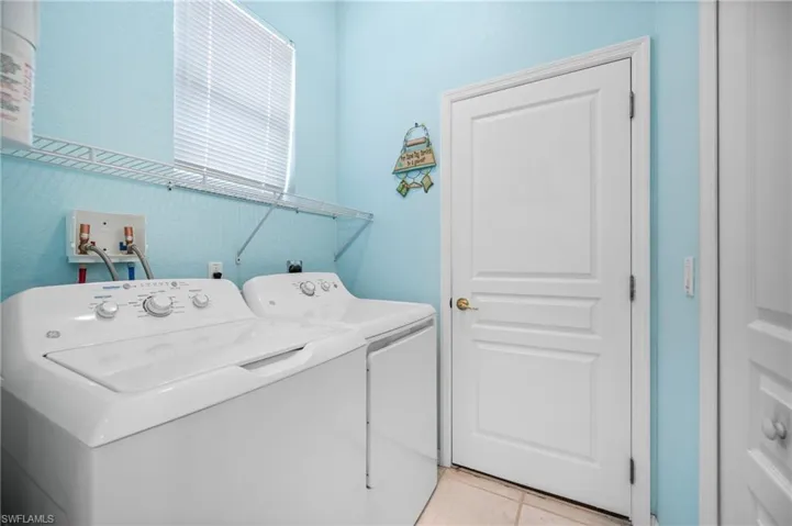 Laundry space featuring a window with blinds, wire shelving, and tile flooring