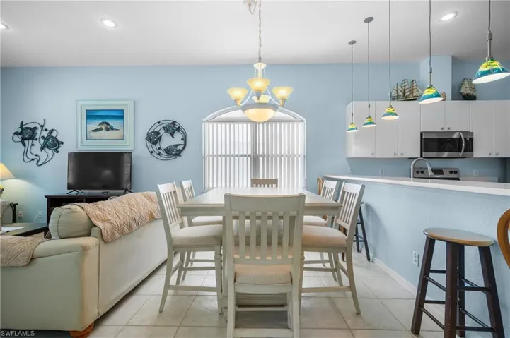 Open-concept living space featuring a dining area with chandelier, kitchen with white cabinetry, stainless steel microwave, and pendant lighting