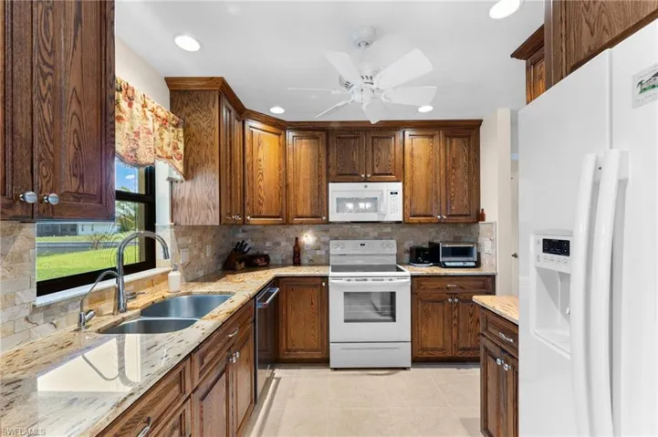 Kitchen with backsplash, ceiling fan, sink, white appliances, and light tile floors