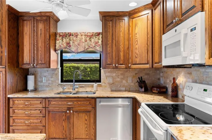 Kitchen with sink, ceiling fan, white appliances, and tasteful backsplash