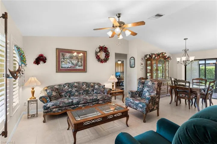 Tiled living room with vaulted ceiling and ceiling fan with notable chandelier