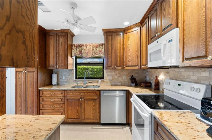 Kitchen with white appliances, sink, tasteful backsplash, ceiling fan, and light tile floors