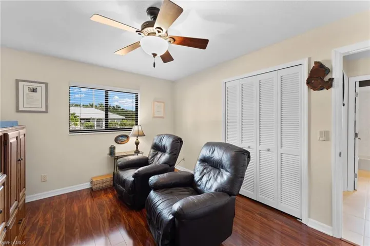 Secondary bedroom currently being used as a sitting room with dark wood-type flooring and ceiling fan