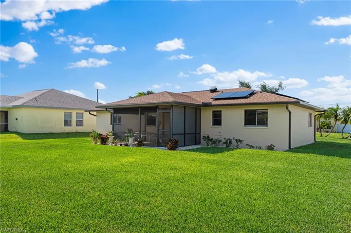 Rear view of house with a sunroom, a lawn, and solar panels