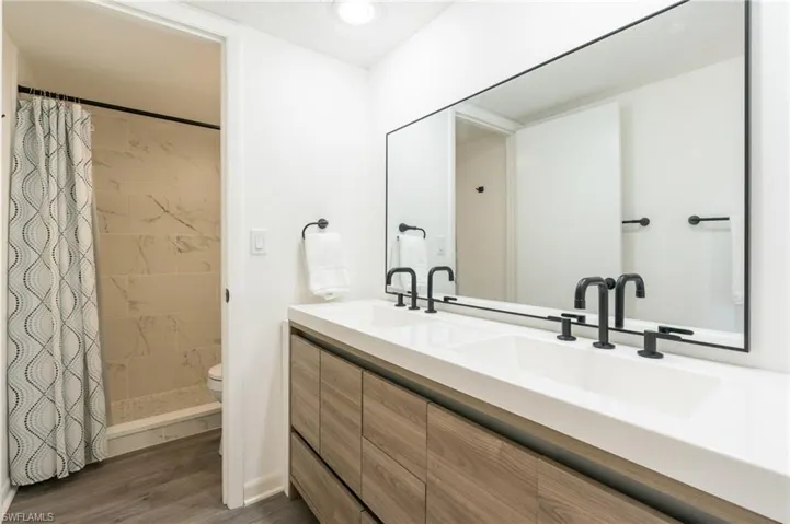 Bathroom with double vanity, a stall shower, and dark wood-style flooring