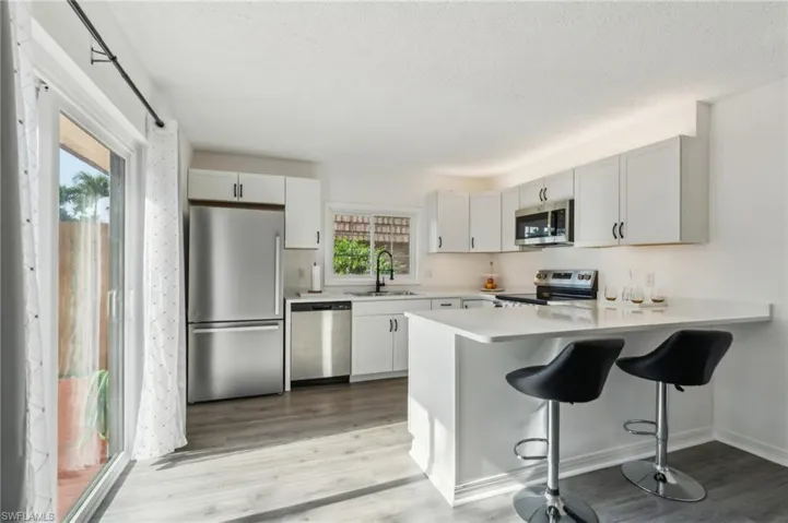 Kitchen with appliances with stainless steel finishes, a peninsula, light wood-type flooring, a breakfast bar area, and white cabinetry