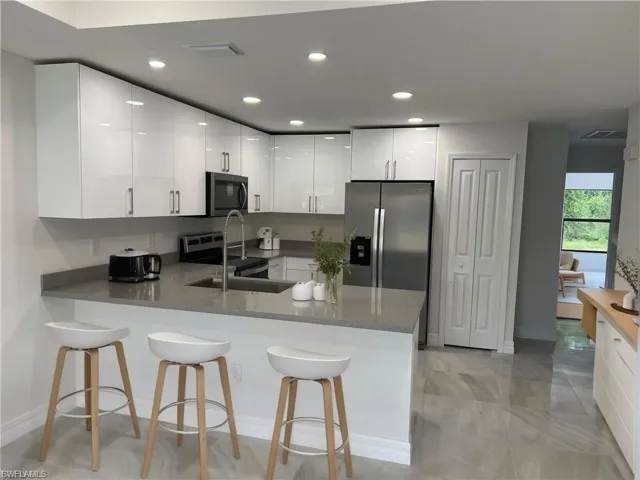 Kitchen with white cabinetry, a kitchen breakfast bar, a peninsula, stainless steel appliances, and modern cabinets