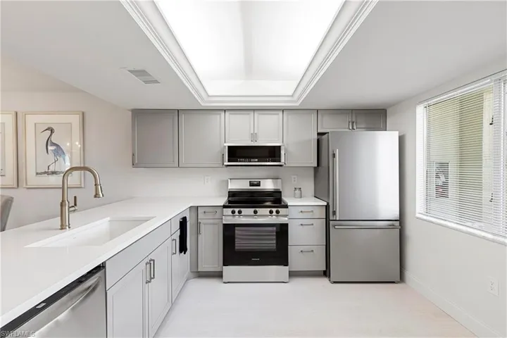 Kitchen with light wood-type flooring, appliances with stainless steel finishes, gray cabinets, sink, and a raised ceiling