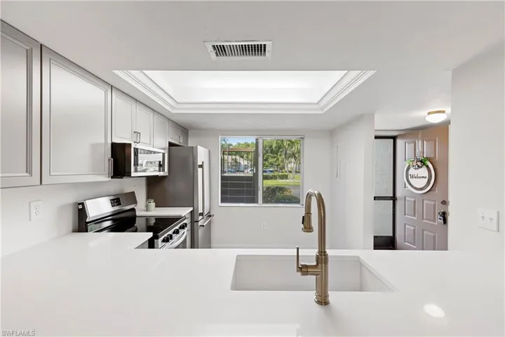 Kitchen with a raised ceiling, sink, stainless steel appliances, and white cabinets