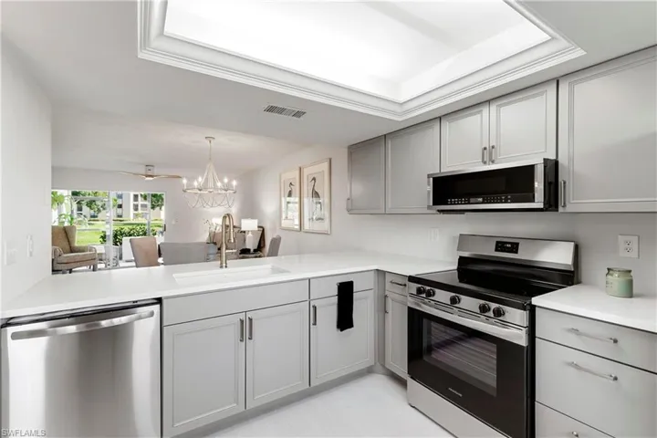 Kitchen with stainless steel appliances, gray cabinets, a notable chandelier, sink, and a raised ceiling