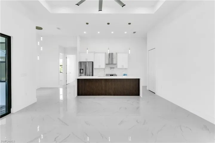 Kitchen with stainless steel fridge, a kitchen island, wall chimney range hood, white cabinetry, and hanging light fixtures