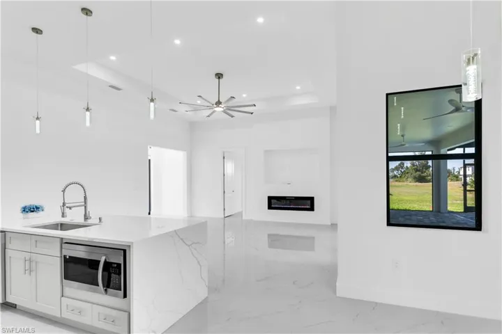 Kitchen featuring light stone counters, sink, decorative light fixtures, white cabinetry, and stainless steel microwave