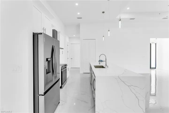 Kitchen with light stone countertops, stainless steel appliances, sink, decorative light fixtures, and white cabinets