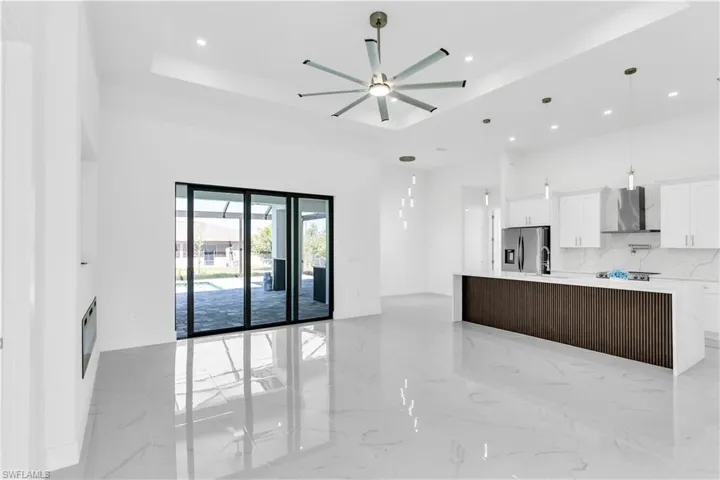 Kitchen with white cabinetry, wall chimney exhaust hood, stainless steel refrigerator with ice dispenser, a spacious island, and a tray ceiling