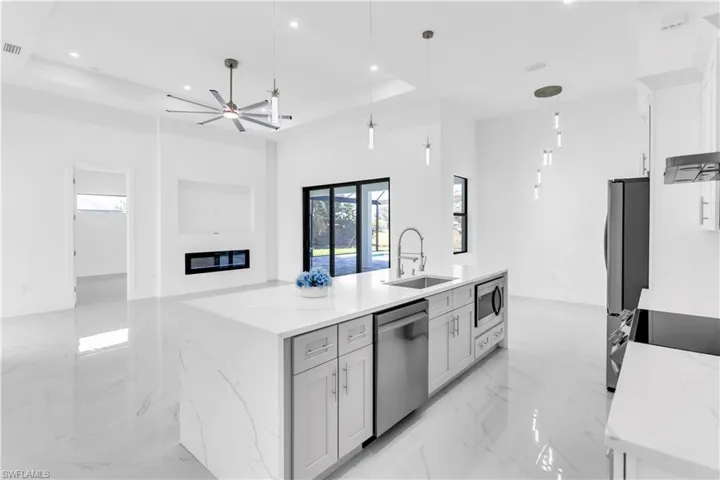Kitchen with light stone countertops, appliances with stainless steel finishes, a raised ceiling, sink, and pendant lighting
