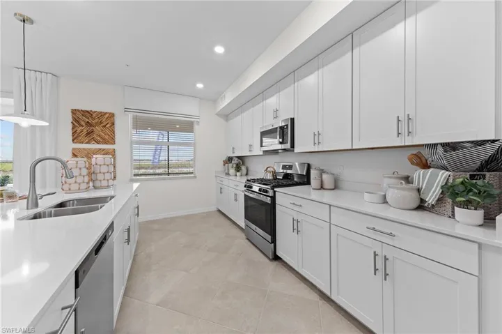 Kitchen featuring hanging light fixtures, white cabinets, appliances with stainless steel finishes, light stone counters, and recessed lighting