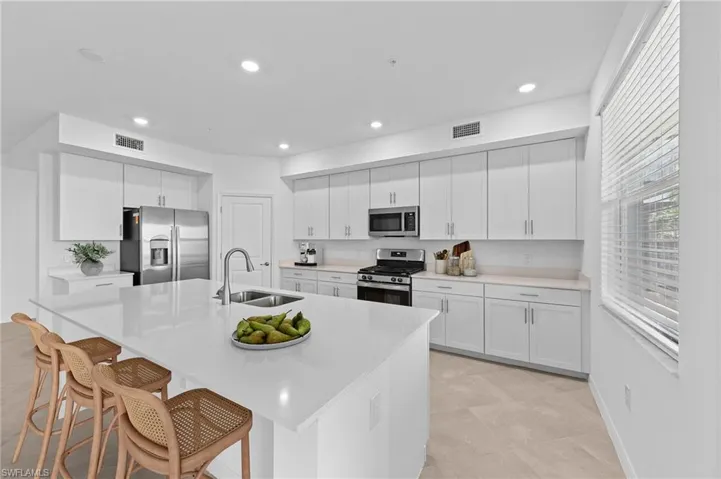 Kitchen featuring white cabinetry, appliances with stainless steel finishes, an island with sink, light stone counters, and recessed lighting