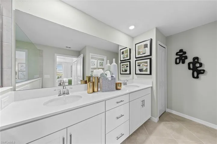 Ensuite bathroom with double vanity, light tile patterned floors, and a closet