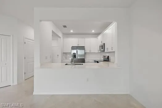 Kitchen with appliances with stainless steel finishes, light countertops, white cabinets, a peninsula, and backsplash