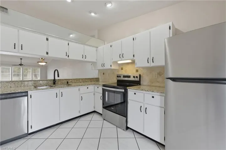 Kitchen featuring stainless steel appliances, white cabinets, light stone counters, and tasteful backsplash