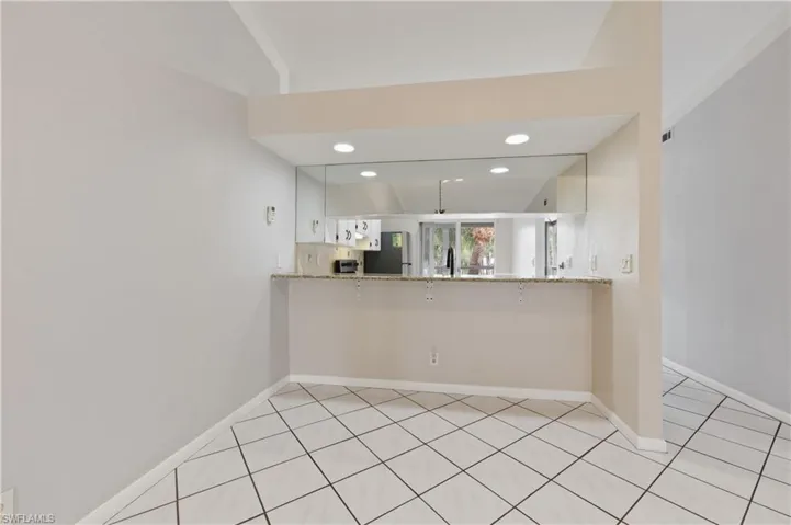 Kitchen with light stone countertops, white cabinetry, a peninsula, freestanding refrigerator, and recessed lighting