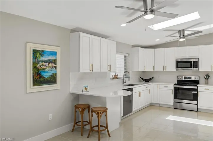 Kitchen featuring appliances with stainless steel finishes, vaulted ceiling with skylight, sink, light tile flooring, and a kitchen bar