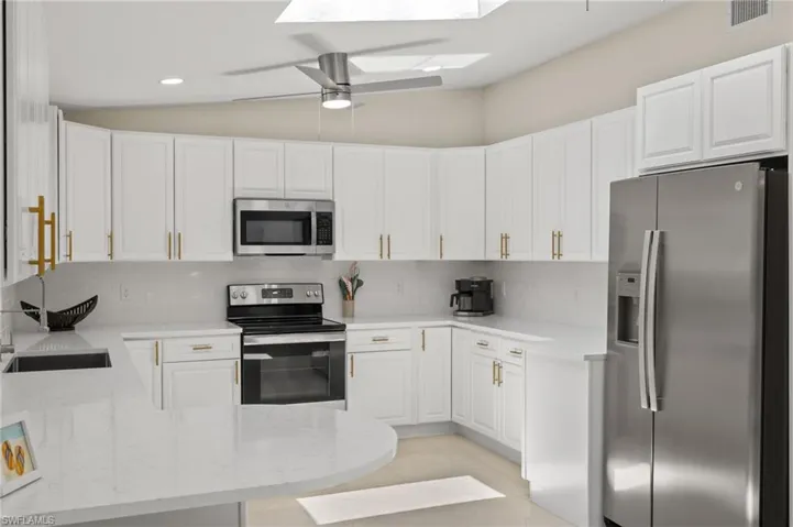 Kitchen with stainless steel appliances, ceiling fan, white cabinetry, light tile floors, and lofted ceiling