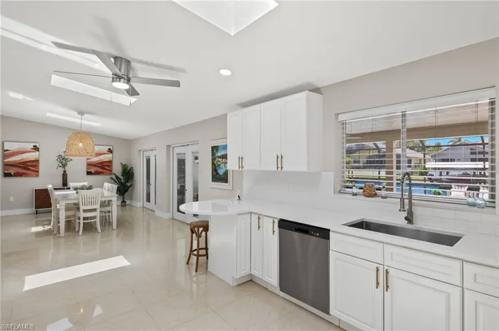 Kitchen with light tile flooring, ceiling fan, stainless steel dishwasher, white cabinets, and sink