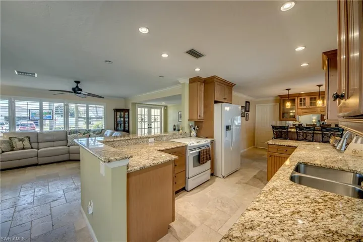 Kitchen with a peninsula, white appliances, ornamental molding, light stone countertops, and open floor plan