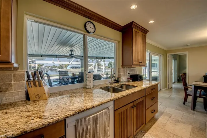 Kitchen with tasteful backsplash, stone tile floors, dishwashing machine, wood finish cabinets, and ornamental molding
