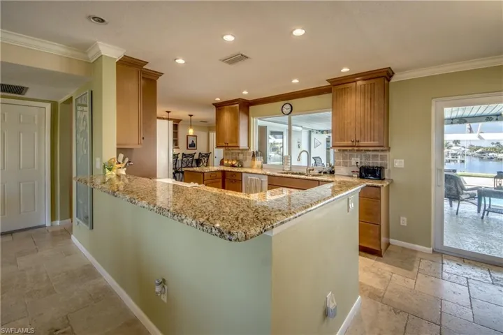 Kitchen featuring stone tile floors, light stone counters, a peninsula, hanging light fixtures, and wood finish cabinets