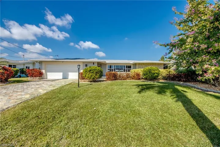 Ranch-style house with a front yard, decorative driveway, stucco siding, and an attached garage