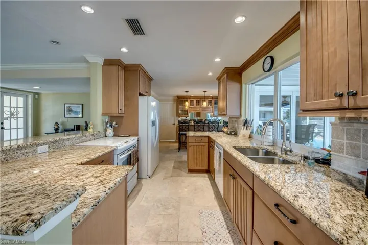 Kitchen with tasteful backsplash, light stone counters, white appliances, crown molding, and a peninsula