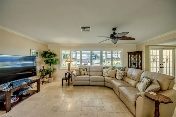Living room with stone tile flooring, french doors, ceiling fan, and ornamental molding