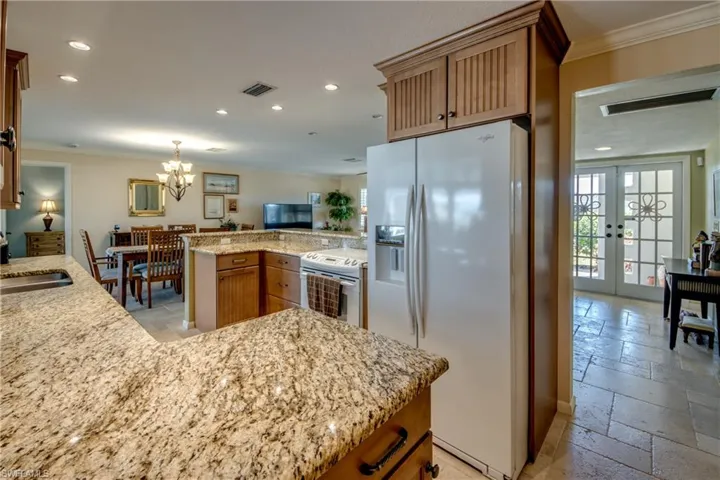 Kitchen featuring wood finish cabinetry, ornamental molding, white appliances, stone tile floors, and light stone counters