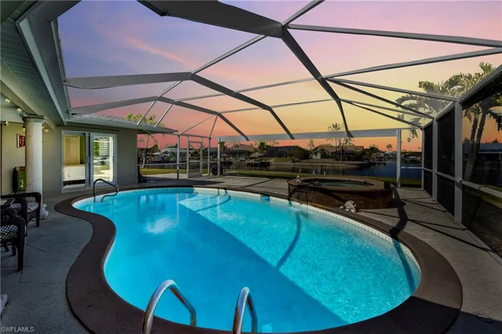 Pool at dusk featuring a sunroom, a patio, glass enclosure, and a pool with connected hot tub