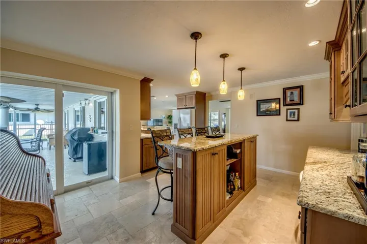 Kitchen featuring wood finish cabinets, a breakfast bar area, light stone countertops, decorative light fixtures, and ornamental molding