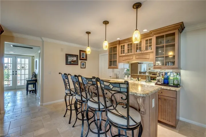 Kitchen with glass fronted cabinets, a kitchen bar, ornamental molding, light stone countertops, and stone tile floors