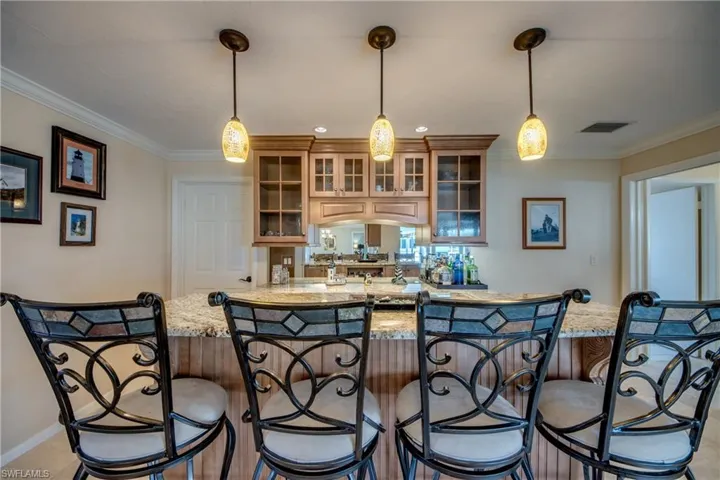 Kitchen featuring glass fronted cabinets, light stone countertops, crown molding, pendant lighting, and a breakfast bar area