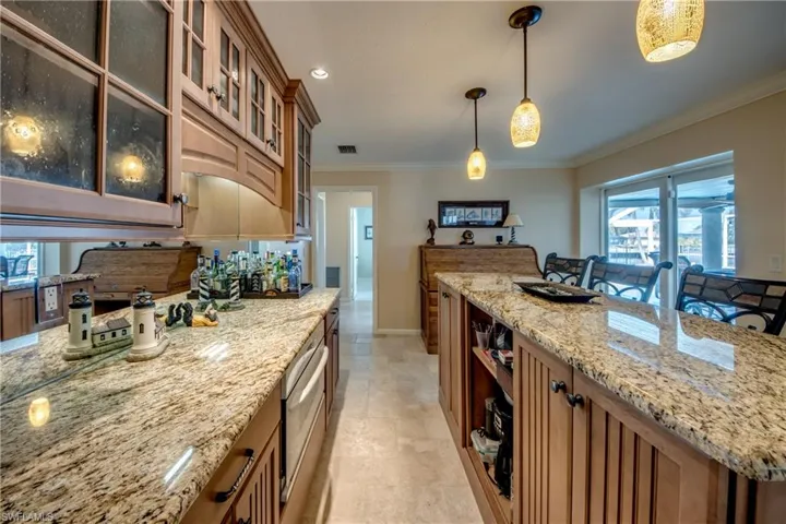 Kitchen featuring plenty of natural light, wood finish cabinetry, light stone counters, and ornamental molding